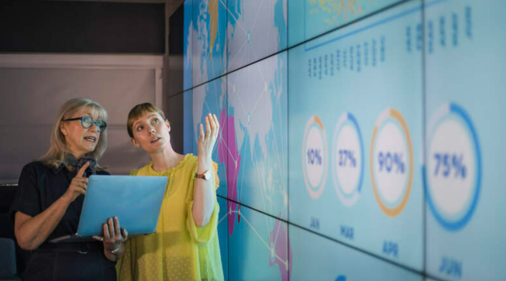 Two women discussing data in front of a dashboard